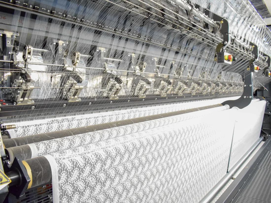 A wide raschel knitting machine producing lace fabric on the Korteks factory floor